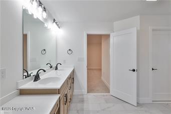 bathroom featuring double vanity, marble finish floor, baseboards, and a sink