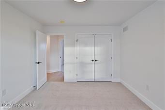 unfurnished bedroom featuring a closet, light colored carpet, visible vents, and baseboards