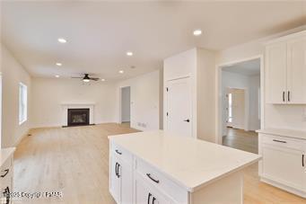 kitchen featuring light wood-style flooring, a fireplace, a kitchen island, white cabinets, and light countertops