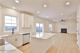 kitchen with a fireplace, a kitchen island, a sink, white cabinets, and dishwasher