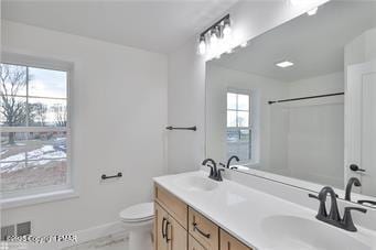 full bathroom with double vanity, a sink, toilet, and baseboards