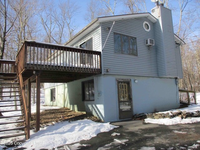 snow covered house featuring a deck, a patio, stairs, a chimney, and a wall mounted air conditioner