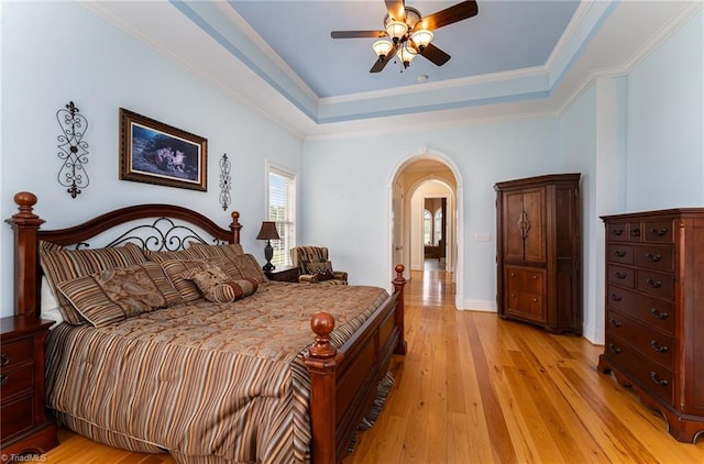 bedroom featuring light hardwood / wood-style floors, ornamental molding, a raised ceiling, and ceiling fan