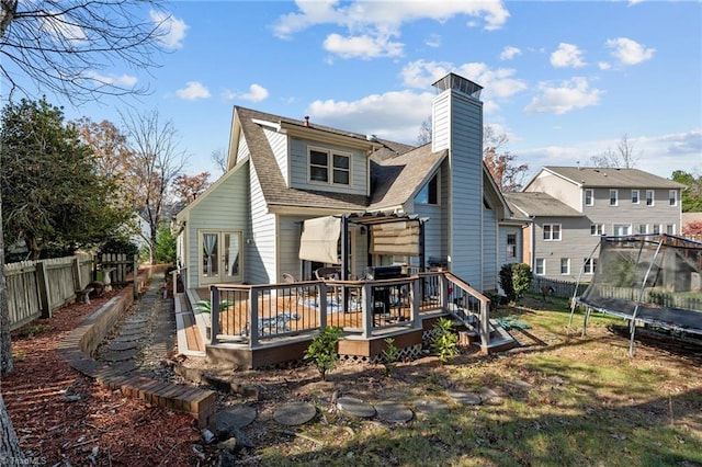 back of property featuring a fenced backyard, a shingled roof, a wooden deck, a trampoline, and a chimney