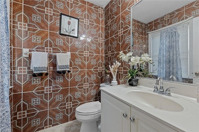 bathroom with a textured ceiling, toilet, vanity, and tile walls