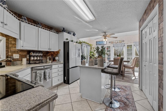 kitchen with light tile patterned floors, white cabinets, a breakfast bar area, appliances with stainless steel finishes, and a sink