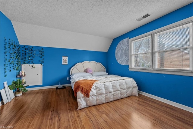 bedroom featuring lofted ceiling, visible vents, baseboards, and wood finished floors