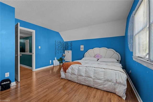 bedroom featuring lofted ceiling, a textured ceiling, wood finished floors, and baseboards