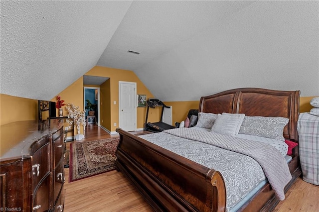 bedroom with lofted ceiling, light wood finished floors, visible vents, and a textured ceiling