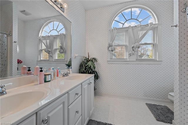 bathroom featuring toilet, wallpapered walls, a wealth of natural light, and a sink