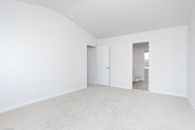 unfurnished bedroom with lofted ceiling, ensuite bath, and light colored carpet