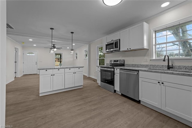 kitchen featuring sink, white cabinetry, stainless steel appliances, light stone counters, and decorative light fixtures