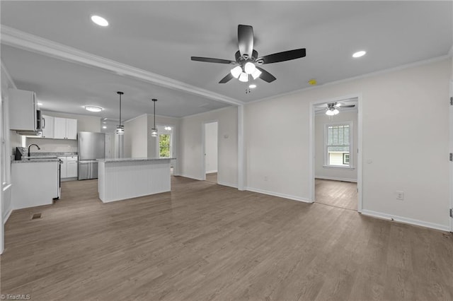 unfurnished living room featuring sink, crown molding, wood-type flooring, and ceiling fan