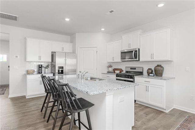 kitchen with stainless steel appliances, a breakfast bar, a kitchen island with sink, tasteful backsplash, and light wood finished floors