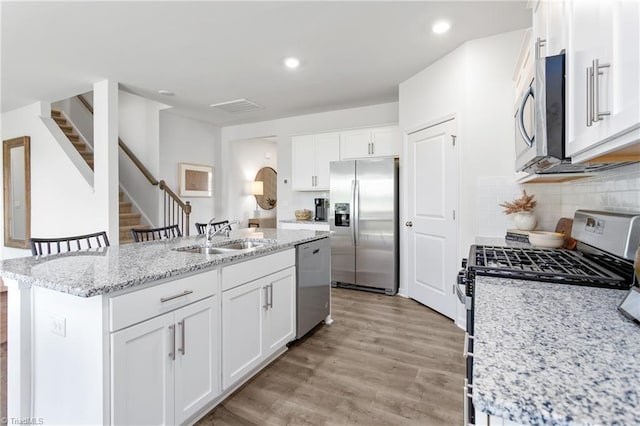kitchen featuring stainless steel appliances, a sink, a center island with sink, white cabinets, and light wood-style flooring