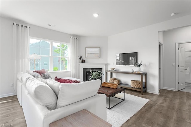 living area featuring wood finished floors, baseboards, a glass covered fireplace, and recessed lighting