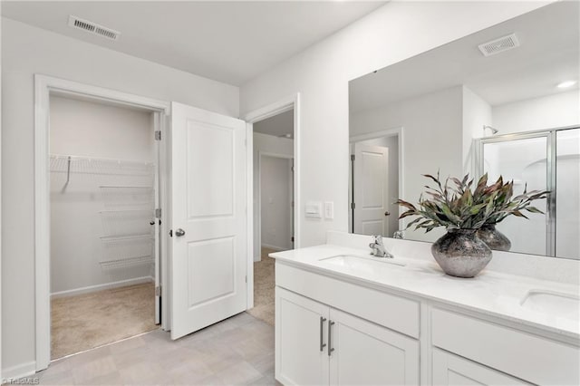 bathroom with tile patterned floors, double vanity, a walk in closet, a stall shower, and baseboards