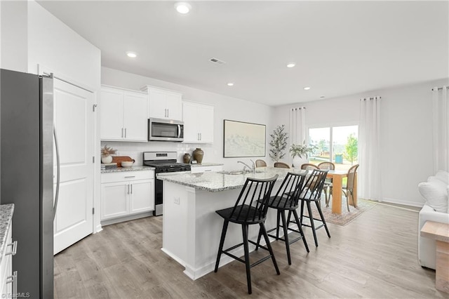 kitchen featuring stainless steel appliances, a kitchen bar, white cabinetry, light wood-style floors, and light stone counters