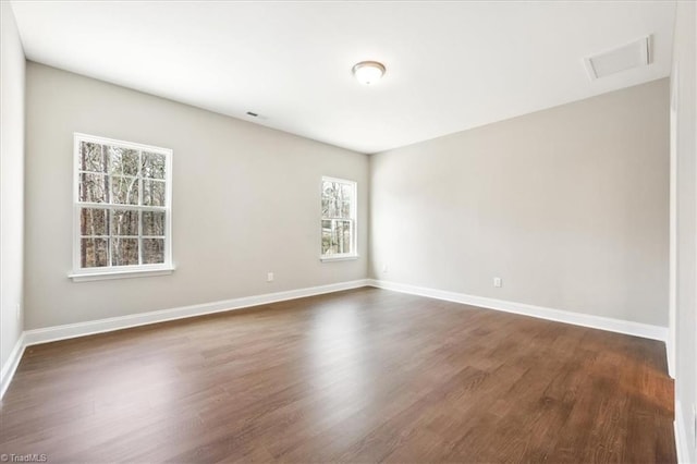 empty room with dark wood-type flooring, a healthy amount of sunlight, visible vents, and baseboards