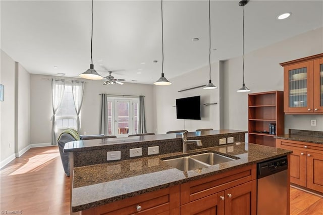 kitchen featuring glass insert cabinets, open floor plan, dark stone countertops, a sink, and stainless steel dishwasher