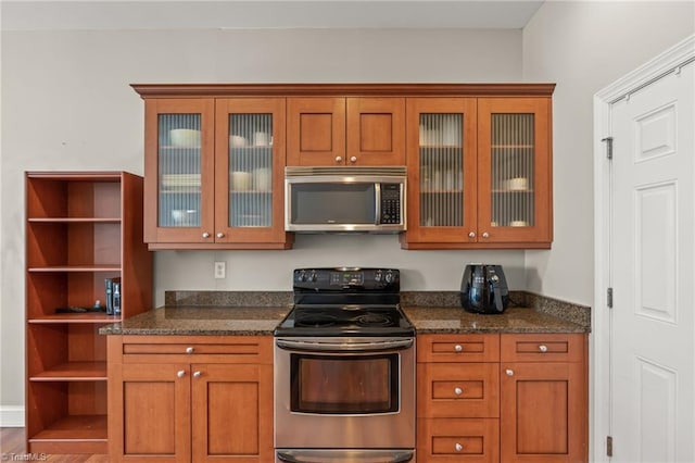 kitchen with open shelves, glass insert cabinets, stainless steel appliances, and dark stone counters