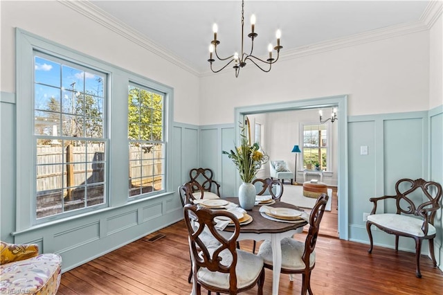 dining room with visible vents, ornamental molding, wood finished floors, a decorative wall, and a notable chandelier