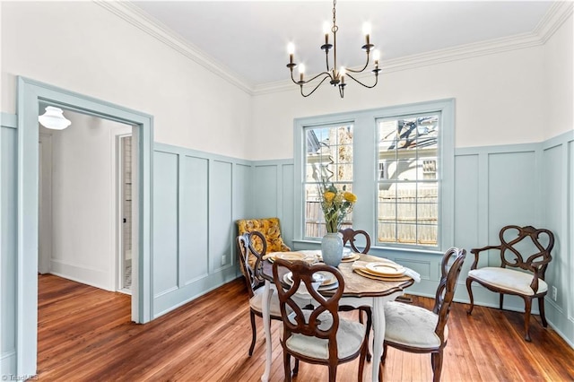 dining area featuring a notable chandelier, ornamental molding, wood finished floors, and a decorative wall