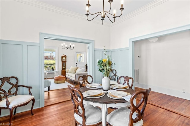 dining area featuring ornamental molding, a decorative wall, wood finished floors, and a notable chandelier