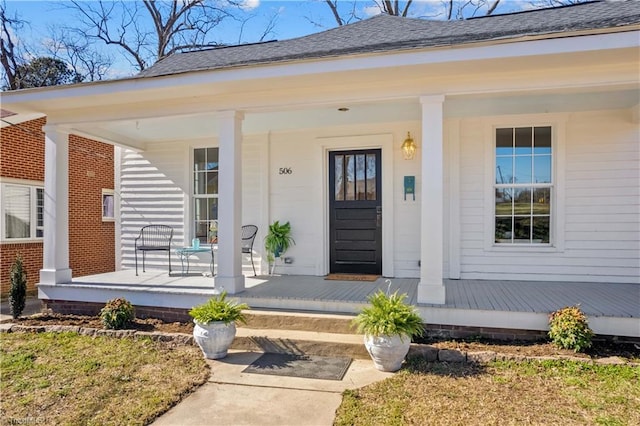 property entrance featuring covered porch and a shingled roof