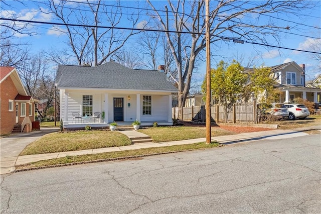 bungalow with roof with shingles, a chimney, a porch, fence, and a front lawn