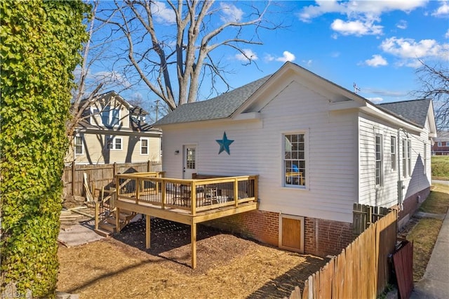 back of property with roof with shingles, fence, a deck, and brick siding