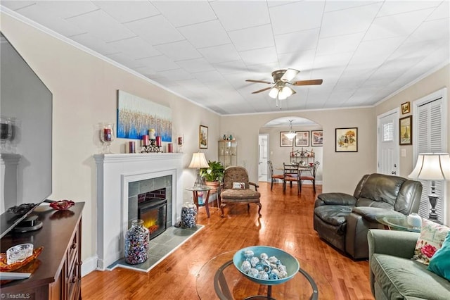 living room featuring ceiling fan, wood-type flooring, crown molding, and a tiled fireplace