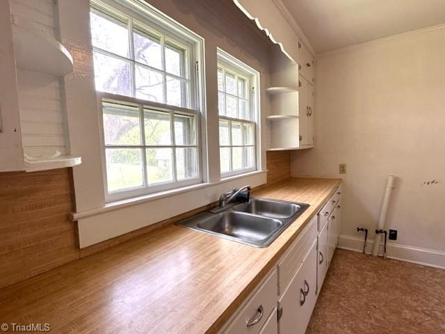 kitchen featuring a sink, white cabinetry, open shelves, light countertops, and baseboards