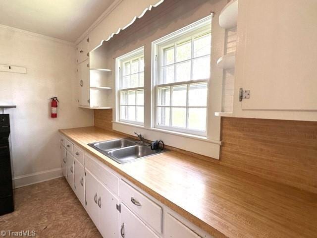 kitchen with a sink, white cabinetry, crown molding, light countertops, and baseboards