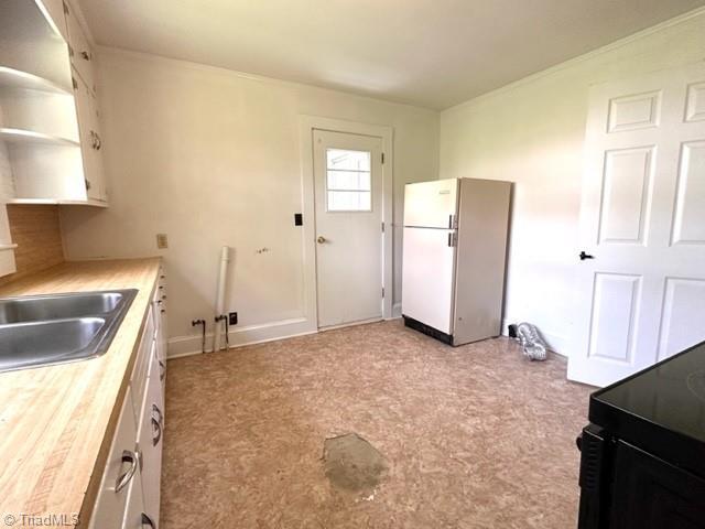 kitchen featuring freestanding refrigerator, a sink, and open shelves