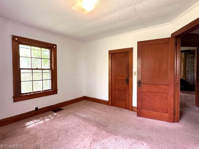 carpeted empty room featuring baseboards, ornamental molding, and a textured ceiling