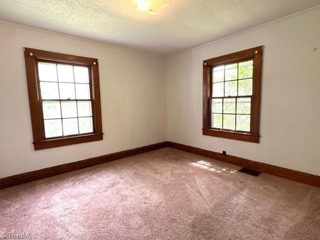 carpeted spare room with a textured ceiling, ornamental molding, and baseboards