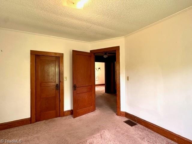 unfurnished room featuring a textured ceiling, light colored carpet, baseboards, and crown molding