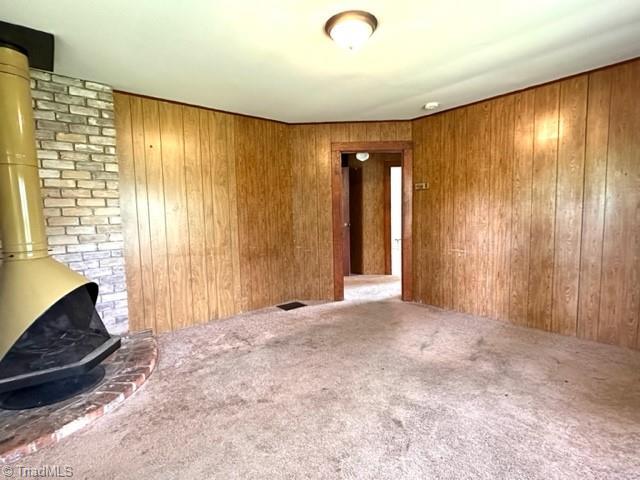 unfurnished living room with a wood stove, carpet floors, and wood walls
