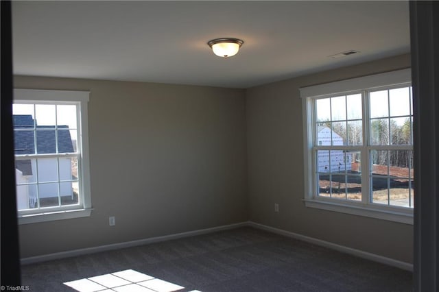 spare room featuring dark carpet and a wealth of natural light