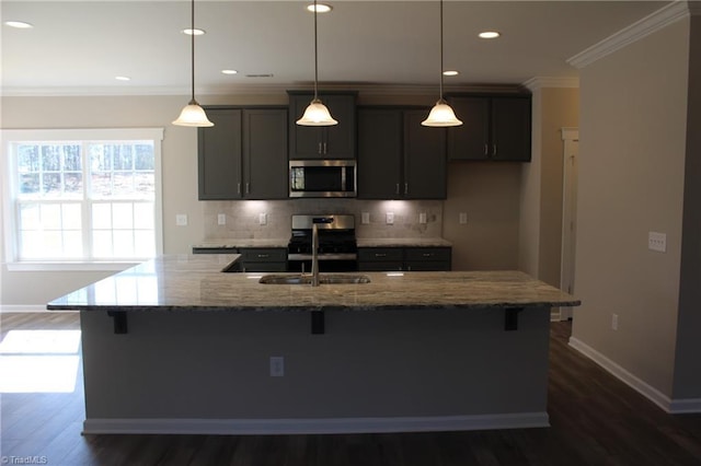 kitchen with appliances with stainless steel finishes, decorative light fixtures, sink, light stone countertops, and a center island with sink