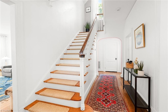 staircase featuring baseboards, a high ceiling, and wood finished floors