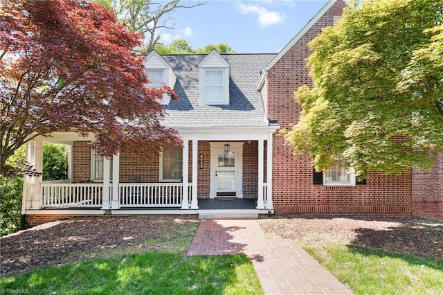 cape cod-style house featuring brick siding, roof with shingles, and covered porch