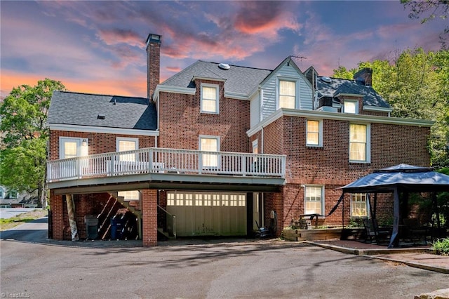 view of front of home with a gazebo, a wooden deck, a chimney, and brick siding