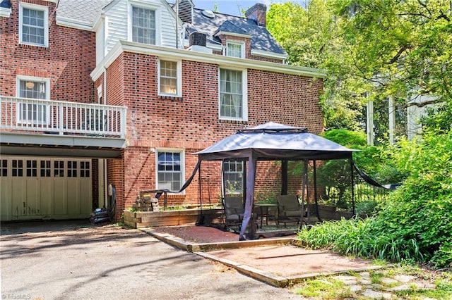 view of front of house featuring a gazebo, brick siding, a garage, a chimney, and driveway