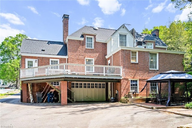view of front of house with driveway, a chimney, a wooden deck, brick siding, and a gazebo