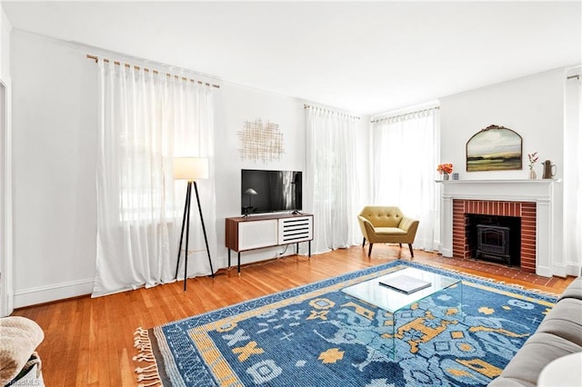 living area featuring a brick fireplace, baseboards, a healthy amount of sunlight, and wood finished floors