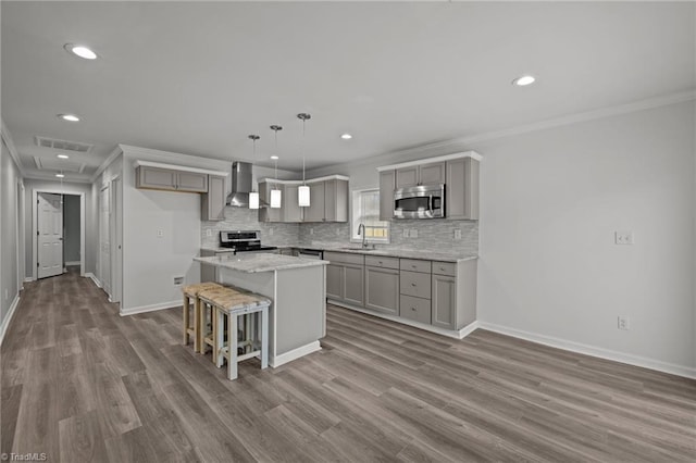 kitchen featuring sink, stainless steel appliances, wall chimney range hood, gray cabinets, and a kitchen island