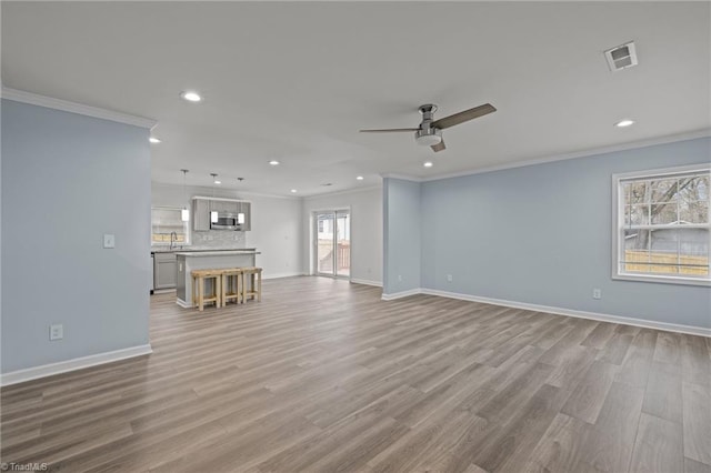 unfurnished living room with crown molding, plenty of natural light, ceiling fan, and light wood-type flooring