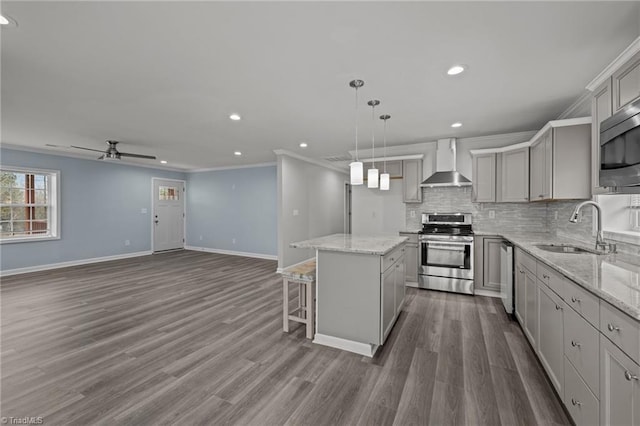 kitchen with appliances with stainless steel finishes, crown molding, wall chimney range hood, gray cabinets, and a kitchen island